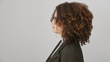 Kıvırcık saçlı, kendine güvenen İspanyol kadın güzel pozlar veriyor, doğal gülüşü, izole beyaz bir arkaplandan yayılıyor.