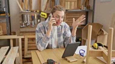 Sıkıntılı genç bir kadın ahşap atölyesinde telefonla konuşuyor. Etrafı alet edevat ve iş parçalarıyla çevrili..