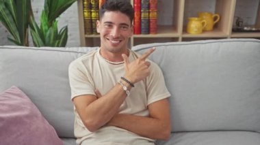 Kapalı alanda, genç, yakışıklı İspanyol adam evdeki kanepede uzanıyor, neşeli gülümsüyor, el hareketi yapıyor, seni sıcak oturma odalarına davet ediyor.