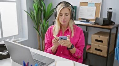 Kafkasyalı bir kadın iş yerinde akıllı telefon kullanırken kulaklıkla müzik dinlemekten zevk alır..