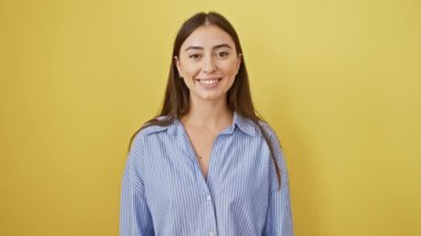 Keyifli, genç İspanyol bir kadın, sıradan bir gömlek giyiyor, kendine güvenen, dişlek bir gülümseme sergiliyor! Sarı bir duvarda poz vermek, keyifli ve pozitif bir tutum sergilemek.