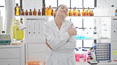 Laboratuvarda kendine sarılan mutlu, kendine güvenen genç bir kadın, gülümseyen mavi gözlerle kendini ifade eden pozitif bir aşk.