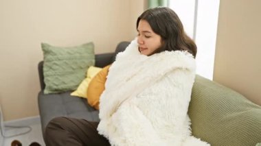 Rahat bir İspanyol genç kadın konforlu, modern bir oturma odasında rahatça uzanır. Huzur ve rahatlık saçar..