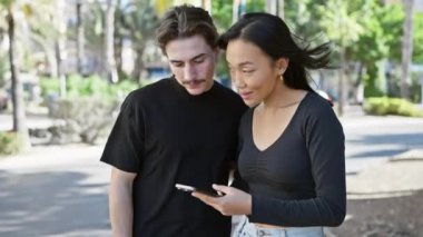 Güneşli bir şehir sokağında akıllı telefon kullanan ırklar arası bir çift..