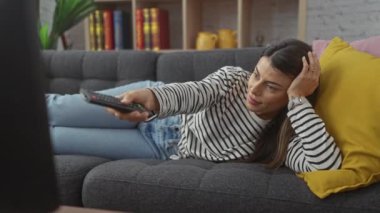 İspanyol kadın rahat oturma odasında uzaktan kumandayla kanepede dinleniyor.