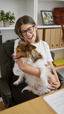 Ofiste köpeği tutan gülümseyen bir kadın, çağdaş bir çalışma alanında arkadaşlık sergiliyor..