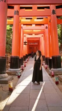 Gözlüklü kendine güvenen İspanyol güzeli, kulaktan kulağa sırıtan, Kyoto 'daki Fushimi tapınağındaki turuncu kırmızı torii tüneline huşu içinde bakan.!
