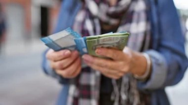 Olgun bir kadın elindeki Şili pezosu banknotlarını bulanık şehir geçmişiyle karşılaştırıyor..