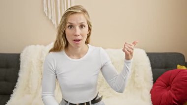 Neşeli genç bir kadın, oturma odasındaki kanepesinden onaylı bir gülümseme yayıyor. Ağzı açık bir şekilde baş parmağını yana uzatıyor. Mutlu günlerin yaklaştığı fikrine güveniyor.!