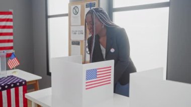 Birleşik Devletler 'deki bir üniversite seçim merkezinde örgü örgülü Afrikalı Amerikalı bir kadın Amerikan bayrağıyla oy kullanıyordu..