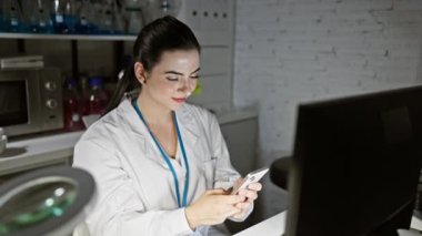 Teçhizatlı bir laboratuvarda akıllı telefon kullanan odaklanmış bir kadın bilim adamı..