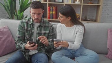 Oturma odasındaki kanepede yan yana otururken akıllı telefonlarla meşgul olan bir adam ve kadın..