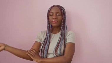 Neşeli Afro-Amerikalı kadın, hayatı kazanan, parmaklarıyla bir Ziyaretçi işareti gösteriyor, pembe arka planda kendine güvenen, ışıldayan gülümsemesi ve göz kırpan yüzüyle.