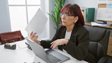 Ofis masasındaki belgeleri inceleyen, profesyonellik duygusunu aktaran, gözlüklü, olgun İspanyol kadın..