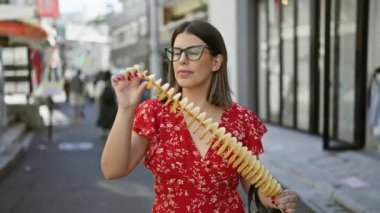 Güzel İspanyol kadın, Takeshita caddesinde, Tokyo 'da bir çubuğun üzerinde neşeyle çıtır çıtır, lezzetli cipsler yiyor. Gezgin abur cubur aşığı, spor gözlüğü ve Japon şehrinde neşeli bir gülümseme.