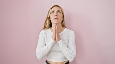 Çaresiz, genç, sarışın bir kadın af diliyor. Elleri birarada dua ediyor. Yüzüne duygu kazınmış. Pembe izole arka planda tek başına duruyor