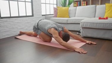 Genç bir adam modern bir oturma odasında pembe bir paspasın üzerinde yoga yapıyor, sağlık ve sükunet sergiliyor..