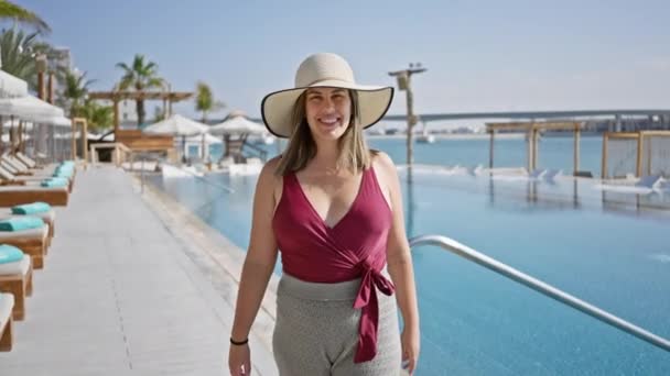 在旅游胜地 一个戴着太阳帽的微笑的女人站在一个装饰着热带棕榈的豪华游泳池边 — 图库视频影像