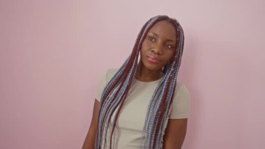 Kendine güvenen Afro-Amerikan kadın dik duruyor, mutlu bir gülümseme ile mesafeyi arıyor, el ele tutuşuyor, pembe bir arka plana yaslanıyor.