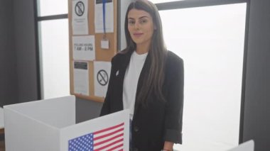 Amerikan seçim kabininde kendine güvenen genç bir İspanyol kadın Amerikan bayrağının yanında onayını veriyor..