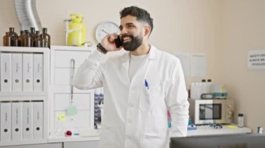 Laboratuvar önlüklü yakışıklı adam laboratuvar ortamında telefonla konuşuyor.