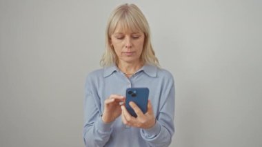 Neşeli sarışın kadın, kendini işaret ederken aynı anda akıllı telefondan mesaj atıyor, saf zevk ve gururla el değmemiş beyaz, izole bir arka planda..