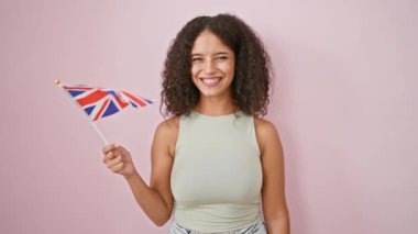 Işıl ışıl genç İspanyol kadın, güzel ve kendinden emin, neşeli bir krallık bayrağı tutan, eğlenceli pembe bir arka planda izole edilmiş