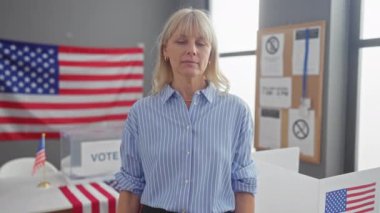 Amerikan oy kullanma merkezinde bayrak taşıyan sarışın bir kadın protesto işareti tutuyor.