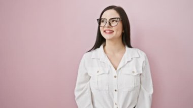 Kendine güvenen genç İspanyol kadın rahat, doğal bir poz veriyor, güzel bir gülümseme yüzünü aydınlatıyor. Profilde duruyor, yana bakıyor, izole edilmiş pembe arka planda..