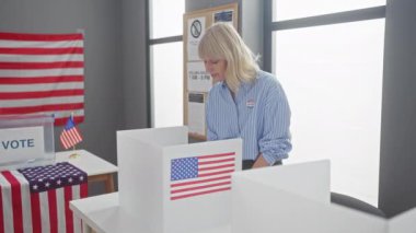 Sarışın bir kadın, Amerikan oy kullanma merkezindeki bir kabinde bayraklarla oy veriyor.