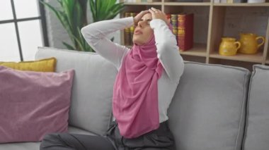 Evine bağlı, depresif genç İspanyol bir kadın kanepenin üzerinde, elleri başının üstünde, yorgun bir yüz ifadesi sergiliyor yoğun migren ağrısı ve strese neden oluyor..