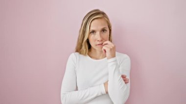 Stresli genç sarışın kadın korkmuş görünüyor, pembe arka planda tırnaklarını yiyor - anksiyete sorunu canlı bir şekilde resmedilmiş