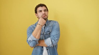 Düşünceli genç bir Arap adam, yüzüne ciddi bir ifade kazınmış, eli çenesine düşünceli, sarı bir arka planda tek başına duran, yoğun şüphe ile kafa karıştırıcı bir fikir üzerinde kafa karıştıran..