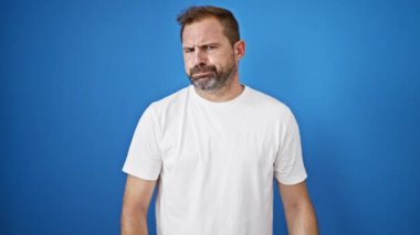 Gri saçlı orta yaşlı bir adam sert mavi bir arka plana karşı baş parmak işareti yapıyor, onaylamıyor..