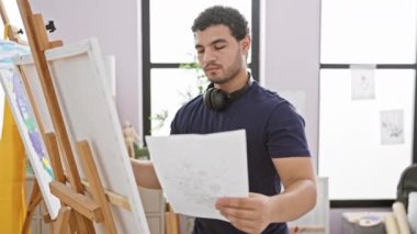 Parlak bir stüdyo ortamında sanat eserlerini inceleyen odaklanmış bir adam yaratıcılığı ve konsantrasyonu somutlaştırıyor..