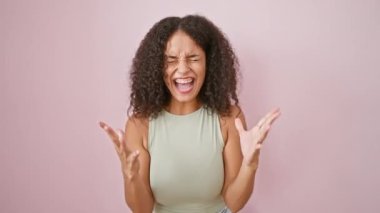 Mutsuz, kıvırcık saçlı, pembe arka planda öfkeyle bağıran, ciddi hayal kırıklığı ve kızgınlığını ifade eden genç İspanyol kadın.