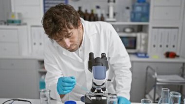 Laboratuvar önlüğü giymiş odaklanmış bir adam, araştırma ve bilimi sembolize eden iyi donanımlı bir laboratuvarda mikroskop kullanır..