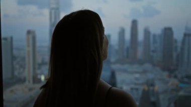 Bir kadının silueti alacakaranlıktaki bir gözlemevinden Dubai siluetine bakıyor..