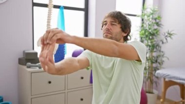 Genç sakallı bir adam rehabilitasyon kliniğinde uzanıyor, kapalı alanlarda terapi egzersizleri yapıyor..