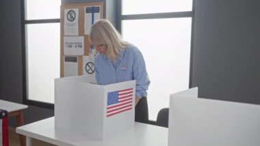 Sarışın bir kadın bir Amerikan seçim okulunda etiket ve bayrağıyla oy veriyor..