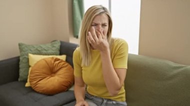 Genç, çekici sarışın kadın iç mekânda tişört giyer. İğrenç, dayanılmaz bir koku evini sarar. Burnum sıkıştı, kokuyu engellemek için nefesimi tutuyorum. Görünür iğrenme.