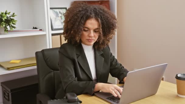一位满头卷发的惊慌失措的年轻女子在办公室里做着多项任务 她用的是手机和笔记本电脑 旁边还有咖啡杯 — 图库视频影像