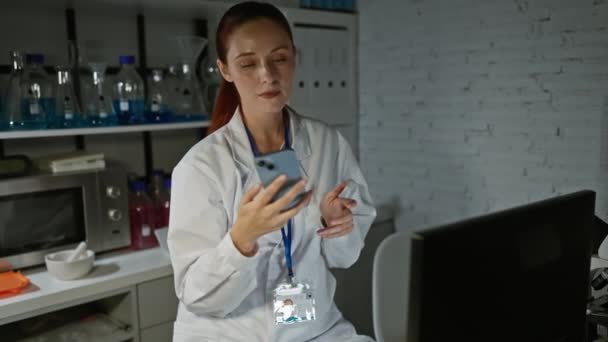 ラボコートの女性科学者が 実験室で携帯電話で話し バックグラウンドに機器やボトルが付いている — ストック動画