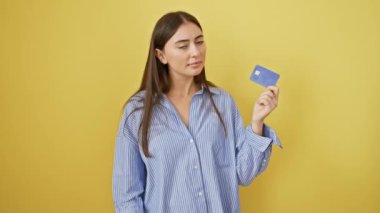 Genç ve güzel İspanyol bir kadın kredi kartı taşıyor. Ciddi bir yüzü var. Eli çenesinde soru sormayı düşünüyor, izole edilmiş sarı arka planda kafa karıştırıcı bir fikir düşünüyor.