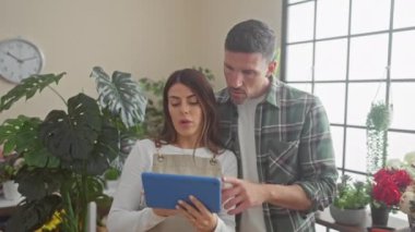 Bir erkek ve kadın, muhtemelen iş arkadaşları, parlak bir çiçekçi dükkanında bir tablet üzerinde işbirliği yapıyorlar..
