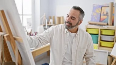 Parlak bir sanat atölyesinde gri saçlı, gülümseyen olgun sakallı adam, yaşlılar için yaratıcılık ve eğlence simgeliyor..