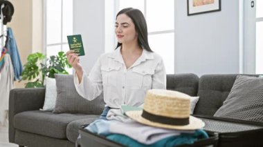 Heyecanlı genç İspanyol kadın, evde oturmuş zaferi kutluyor, neşeyle gülümsüyor, güzel Suudi Arabistan pasaportunu yükseltiyor, zaferle ve başarıyla ışıldıyor..