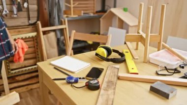 Orta yaşlı bir kadın marangozluk atölyesinde aletler ve güvenlik teçhizatlarıyla not alıyor..