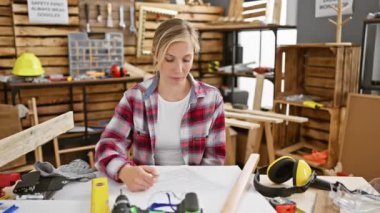 Şok olmuş genç sarışın marangoz kadın, heyecan verici sürpriz karşılaşma marangozluk masasında otururken şaşkınlık ve korku uyandırıyor.