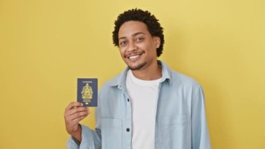 Kendine güvenen Afro-Amerikan erkeği, gülümseyen dişlek gülümsemeli, Kanada pasaportlu, sarı arka planda izole edilmiş.